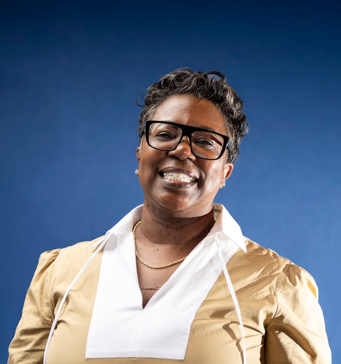 Portrait of a smiling woman with glasses in business attire against a blue background.