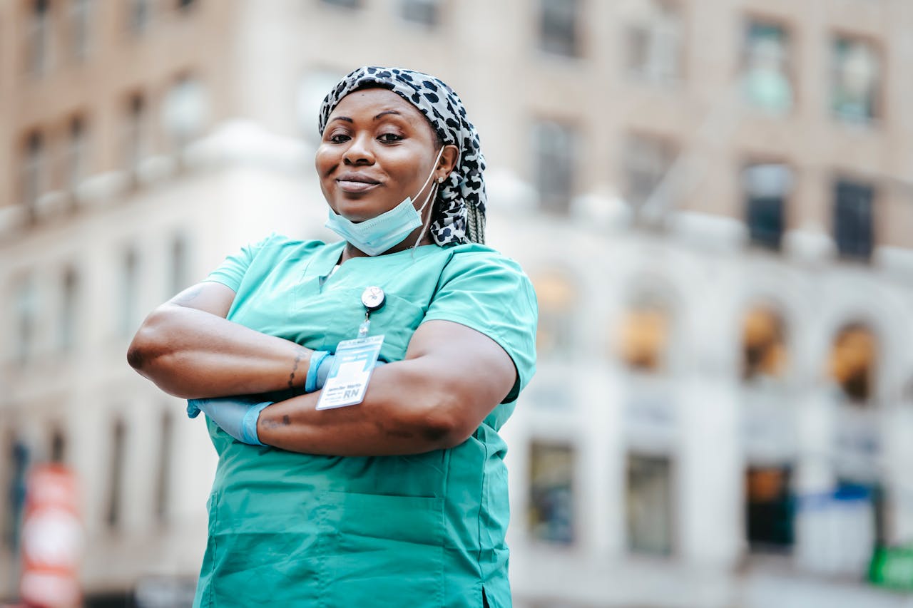 Proud nurse with arms crossed, in uniform, outdoors, urban setting, showing confidence and professionalism.
