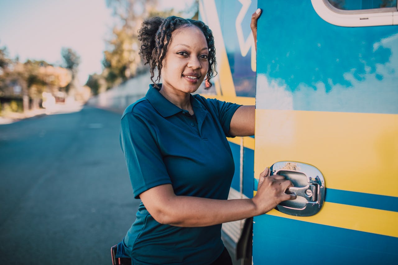 Smiling female paramedic stands confidently beside an ambulance vehicle outdoors.